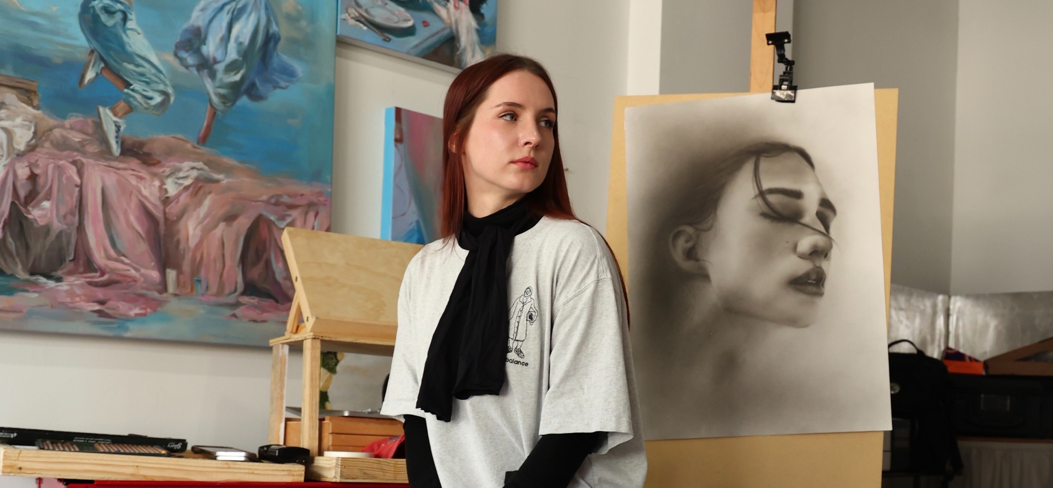 Viktoriia Levina in her studio beside an oil painting and a charcoal portrait